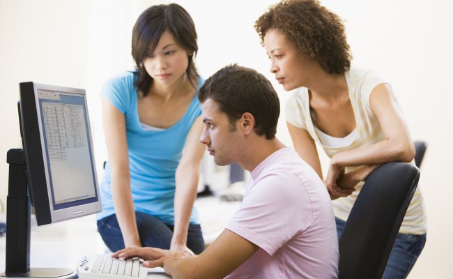 Three people sitting in computer room looking at monitor